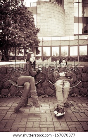 vintage style portrait of two teenager sitting on iron chairs.