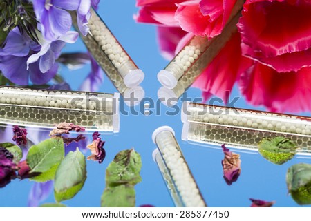 small glass tubes with homeopathy globules and flowers, laying on a mirror