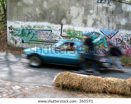 Two skaters being pulled by a car infront of graffiti