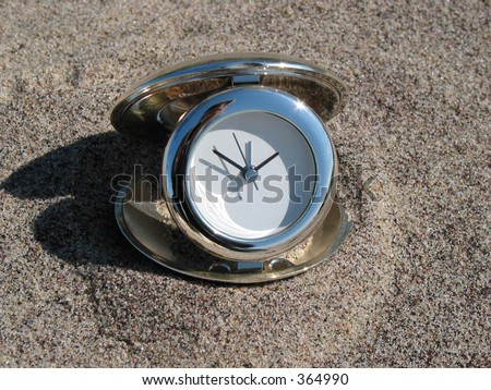 Chrome clock lying on the beach with a surfer in the background