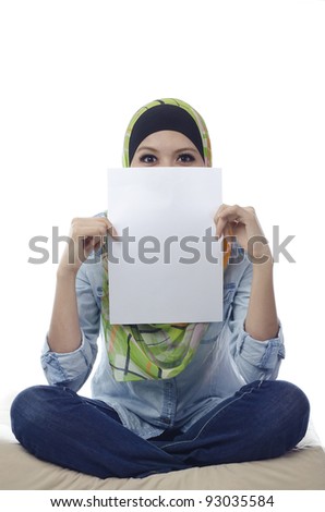 Beautiful young muslim woman seat and holding a blank paper.half face covered by blank paper