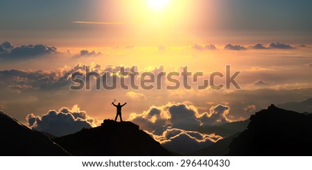 A man standing on the top of the mountain above the clouds with ice axe in his hands.