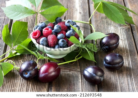 Group of fresh plums, blueberry and raspberry on wood background