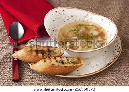 A chicken broth in white ware on burlap tablecloth