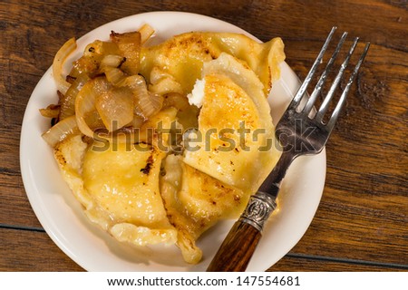 A plate of handmade pierogi with a side of carmelized onions.  There is a decorateive silver and wood fork on the plate.  Everything is shot on a wood table.
