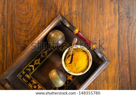 Ceramic bowl filled with yellow curry powder with a wood spoon on a decorative wooden tray. The tray is shot on a wood surface.