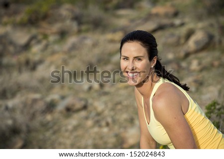Young woman smiling for the camera while stretching to warm up for a trail run outdoors at South Mountain Park in Phoenix, Arizona.