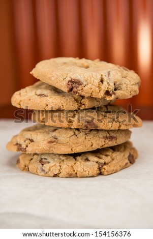 A stack of five fresh delicious chocolate chip cookies.  Shot on white parchment paper with corrugated tin in the background.