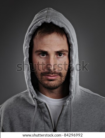 Portrait of a young male model wearing a gray hoodie and white t-shirt.  He has a serious expression and is shot on a gray background.