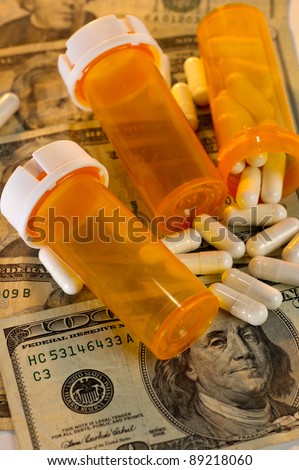 Open bottle of pills spilling out on top of US currency, along with empty bottles. Showing how much less one gets for the money when it comes to the rising cost of health care.