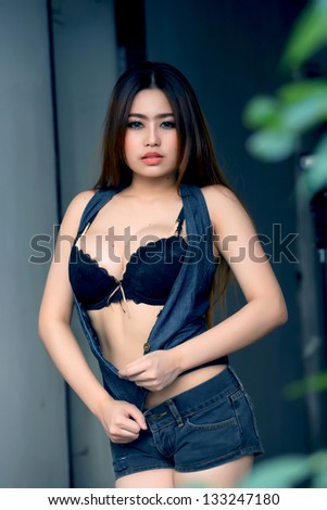 Young beautiful Asian woman in black lingerie with vest and short pants jeans, voluptuous posing outdoors