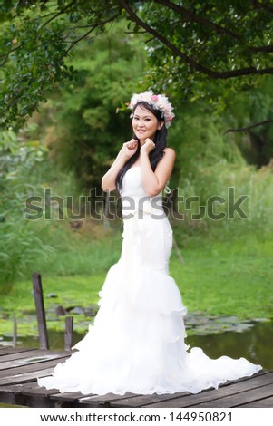 Beautiful Asian lady in white bride dress, posing in the forest, greenery in the background, model is Thai Ethnicity.