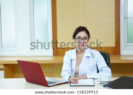 Attractive young female doctor sitting at desk in office doing paperwork.