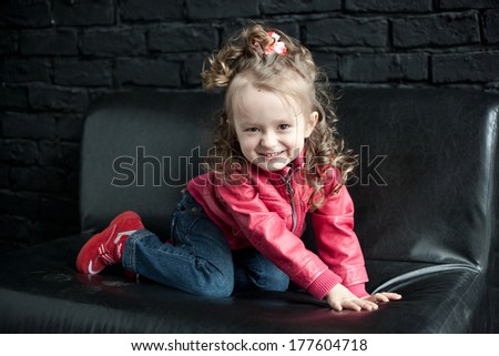 little girl in leather red rock star jacket on black sofa smiling and playing