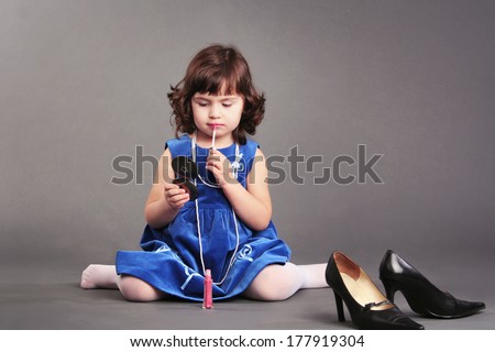 little girl trying her mothers cosmetic lipstick with mothers high heels shoes