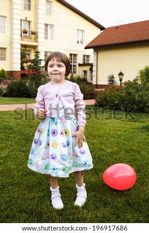 little blond girl in the mansion house garden with red ball