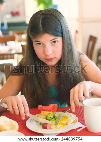 preteen beautiful girl with long dark hair have breakfast in the all inclusive restaurant