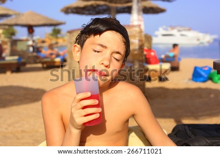 preteen handsome sun tanned boy drink summer orange shake coctail with straw