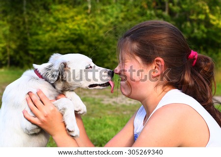 white puppy lick teen girl at face on the summer nature background