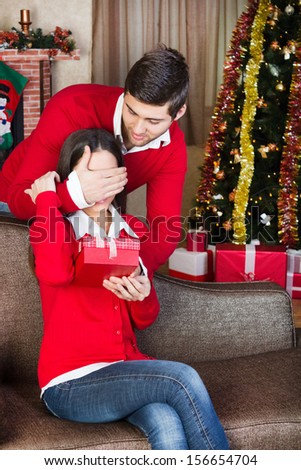 man covering woman\'s eyes with his hand and surprising  with a gift on christmas Eve