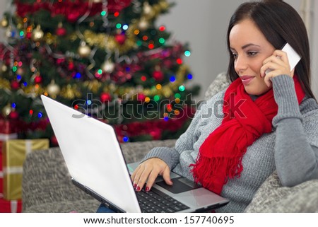 Smiling young woman with laptop sitting near Christmas tree