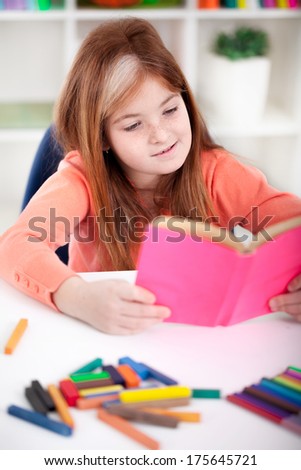 cute little red-haired girl reading a book at home