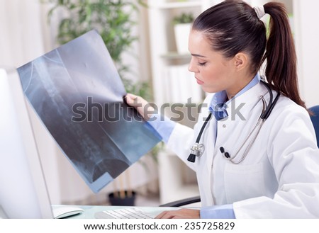 young female radiologist  looking at x-ray and  types report  into the computer