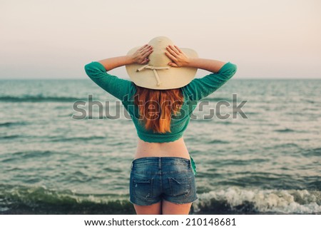 red haired woman in a wide sun hat enjoying the sunset at the beach