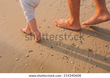 father helps to make the child\'s first steps on the beach