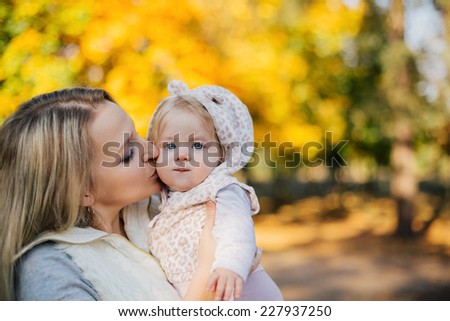 Young mother kissing her baby daughter in autumn park