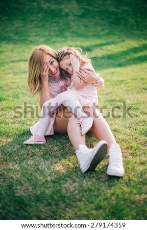 Happy family. Mother and daughter playing and hiding faces while sitting on grass