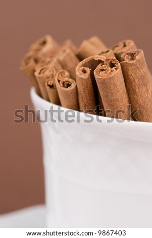 Close-up of a coffee cup filled with cinnamon sticks on brown background