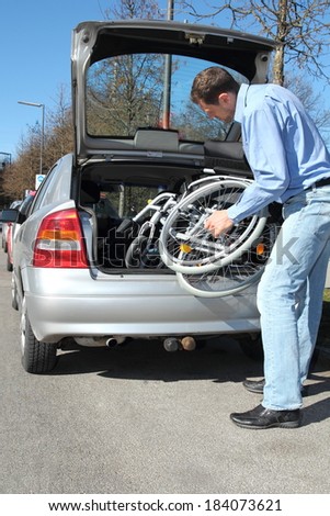 Man packing a wheelchair in a car\'s trunk