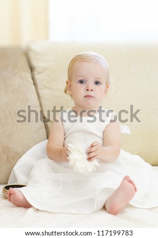 Little, blond baby girl getting ready for the celebration and dressing up in jewelry. Baby dressed in a white fluffy dress, bracelet, bow. Dress up
