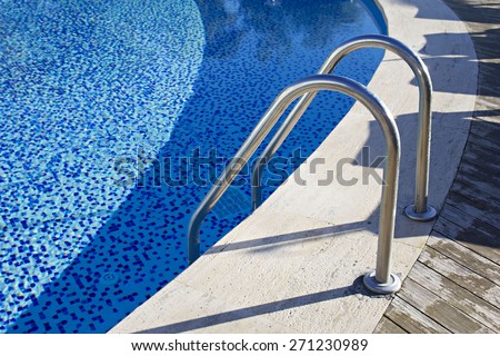 Hotel swimming pool. Grab bars ladder in the blue swimming pool. Sunbeds