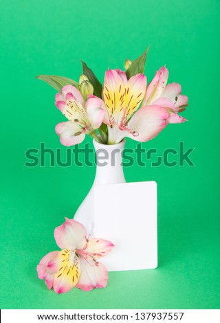 Flower of an alstroemeria and empty card near a vase, on a green background