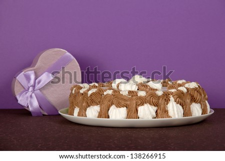 Dish with a biscuit, a gift a heart on a brown cloth, on a violet background