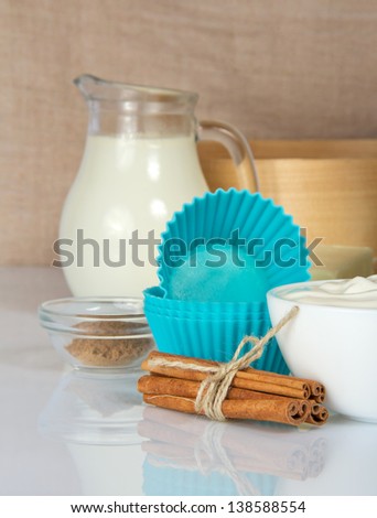 Cinnamon sticks, milk, sour cream and a cake pan, on a beige canvas
