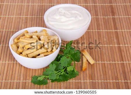 Against a bamboo cloth a bowl with sour cream, a bowl with toasts and parsley