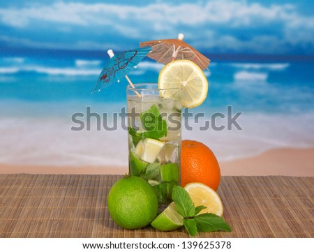 Mojito with umbrellas, orange, a juicy lime, a lemon on a bamboo cloth against the sea