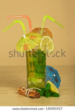 Drink with straws is decorated with umbrellas and cinnamon sticks tied up by a rope, on the beige