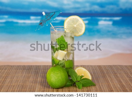 Mojito, a juicy lime, a lemon slice, on a bamboo cloth against the sea