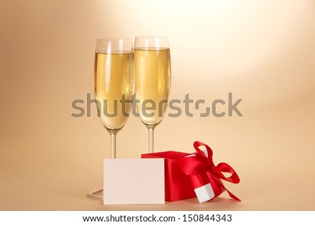 Two wine glasses with champagne, a small gift box with an open cover and blank card on a beige background