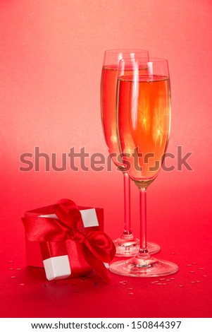 Two wine glasses with champagne and a small gift box with an open cover on a red background