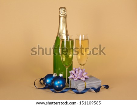 Bottle and wine glasses with champagne, a gift box with a bow, Christmas toys and a serpentine on a beige background