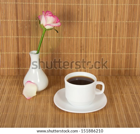 Vase with a rose and a cup with drink against a bamboo cloth