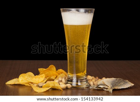 Glass of foamy beer with bubbles, chips, salty fish and the pistachios on the table
