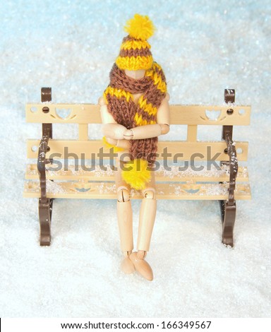 Wooden man sits on a snow-covered bench
