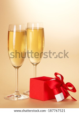 Two wine glasses with champagne and a small gift box with an open cover on a beige background