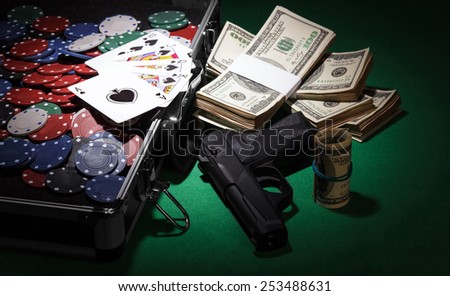 Poker chips and dollar Money bills in case and gun on green cloth
